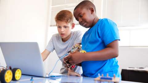 교실 작업대에 서 있는 중학생 두 명이 앞에 있는 노트북으로 연결된 Arduino 장치를 프로그래밍하면서 협업하고 있습니다.